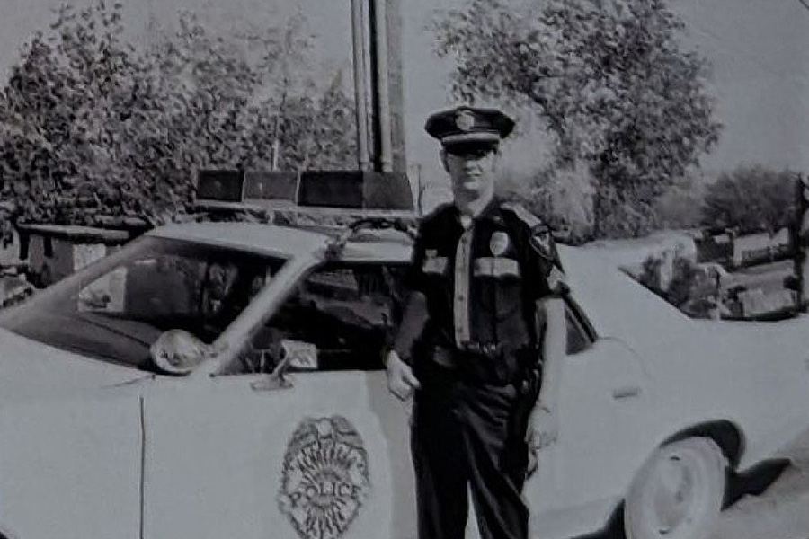 An Old Image in Black & White of a Henderson Police Officer Beside a Police Car in the 1960s